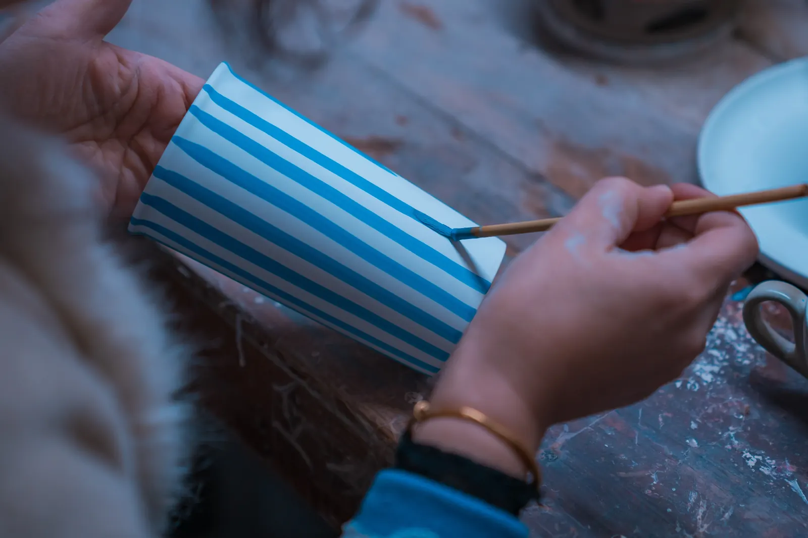 A hand brushing stripes onto a Millie cup in the workshop