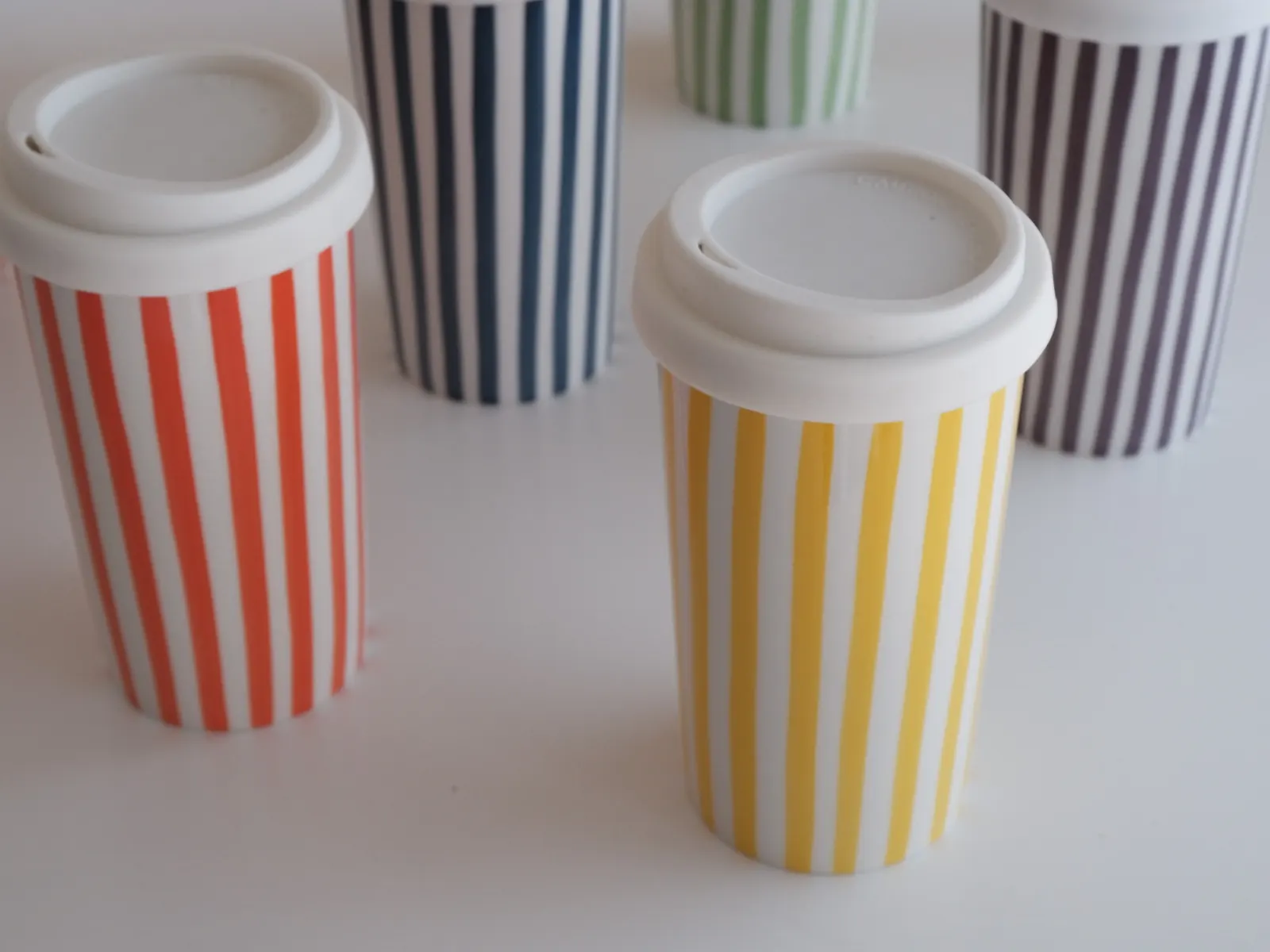 Several striped Millie cups with lids on a white table